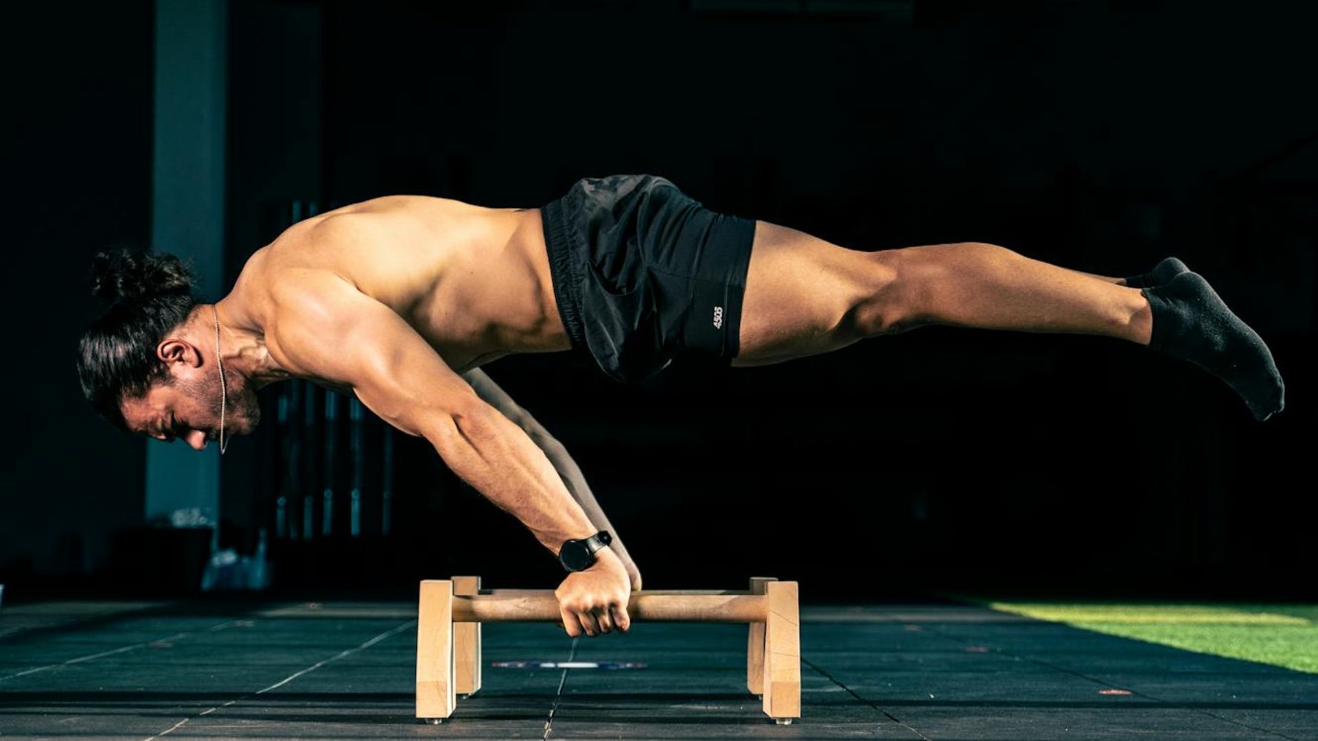 Man performing a controlled bodyweight exercise in a minimalist dark gym.
